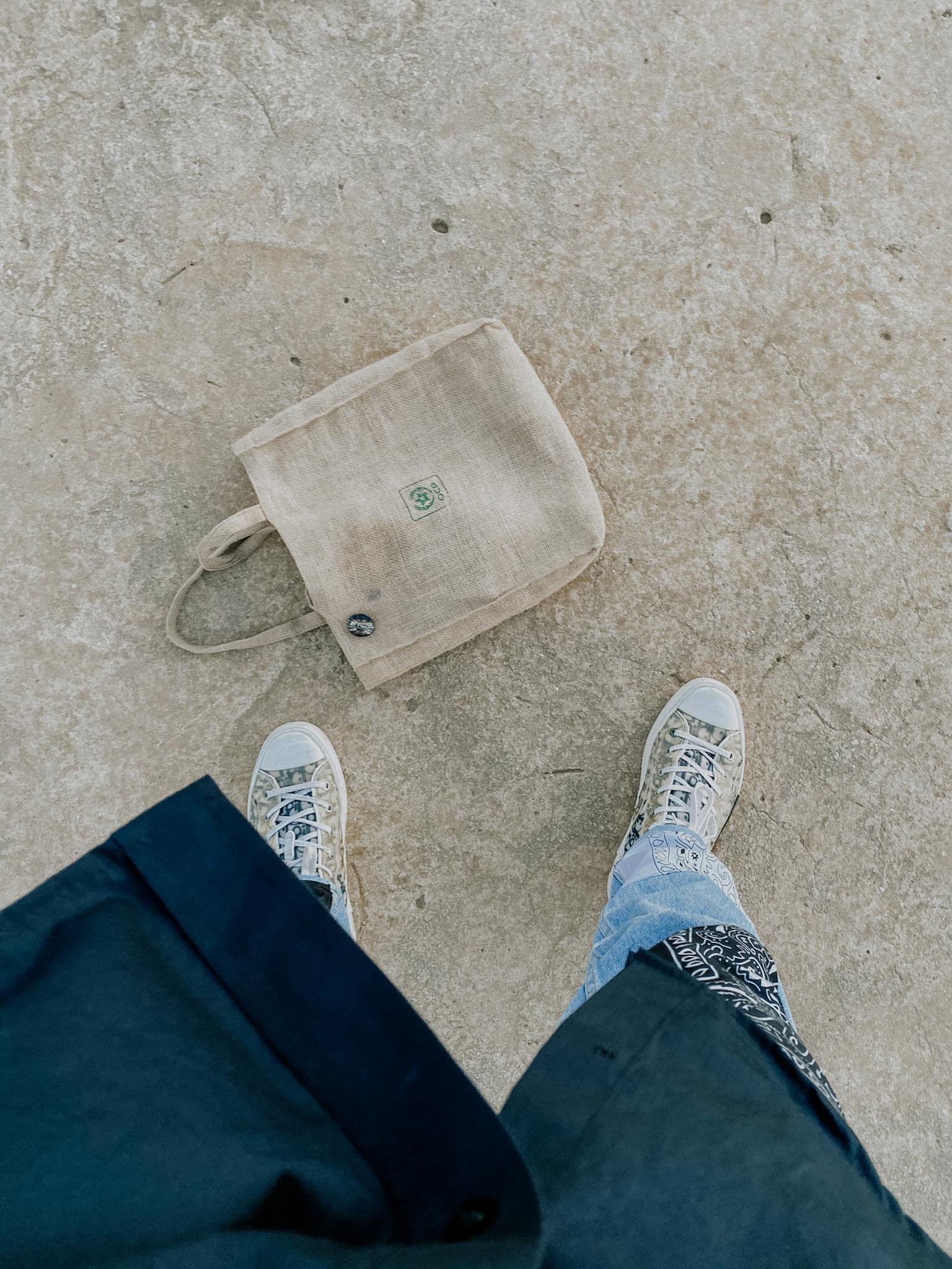 Top view of person in sneakers standing on pavement with eco-friendly bag.