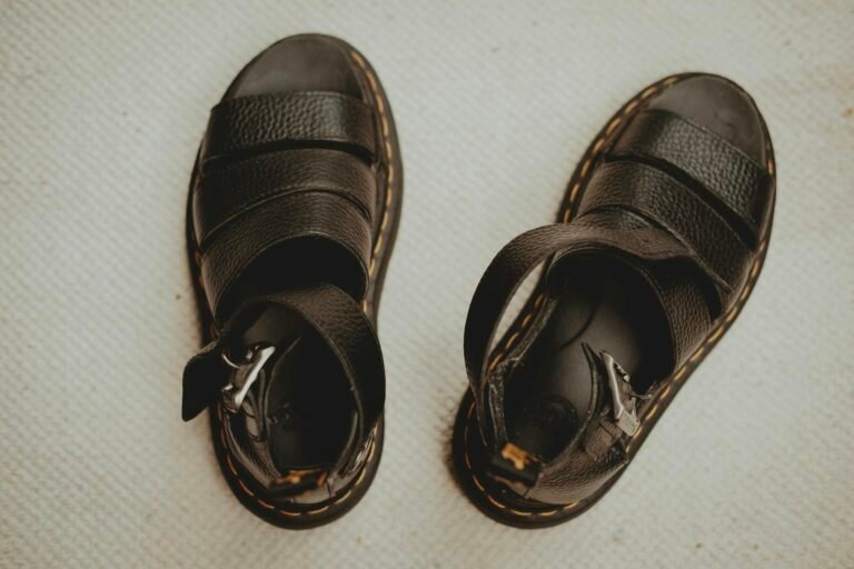 Close-up of black leather sandals with buckle straps on a textured beige surface.